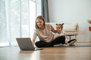 Using laptop. Young woman with little girl are doing yoga at home