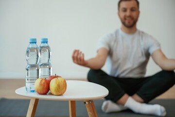 Bottles of water and apples. Yoga man is sitting on a mat at home