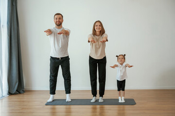 Warm up exercises. Family of mother, father and daughter are doing yoga at home