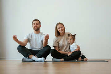 Cheerful people. Family of mother, father and daughter are doing yoga at home
