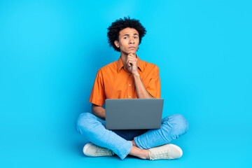 Full length photo of handsome uncertain guy wear orange shirt reading modern gadget emtpy space isolated blue color background