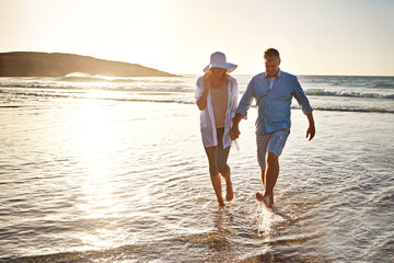 Senior couple, playing and holding hands with beach sunset for love, embrace or bonding together in nature. Man, woman or lovers enjoying outdoor fun or summer holiday by water, sea or ocean coast