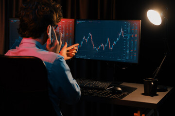 Young investor stock trader calling with broker to invest earning highest profit on current market graph online in real time at neon light modern office, monitor showing investment exchange. Gusher.