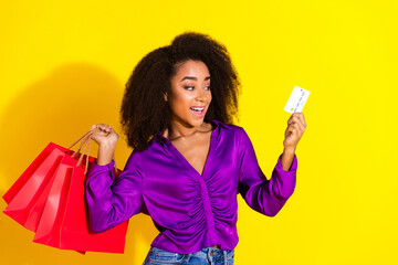 Photo portrait of attractive young woman hold shopping bags credit card dressed stylish violet clothes isolated on yellow color background
