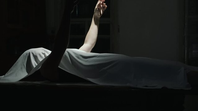 Dead body covered with a white cloth in the darkroom with swinging a light