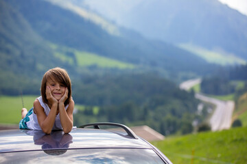 Cute child, boy sitting on a car ceiling, meditating enjoying the quietness of nature, travel on the road to scenic mountains