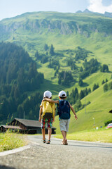 Two little children, boy brothers with backpacks travel on the road to scenic mountains