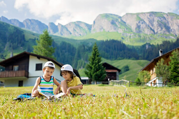 Two cute children, reading a book on a lawn in Swiss alps