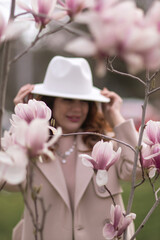 Woman magnolia flowers, surrounded by blossoming trees., hair down, white hat, wearing a light...