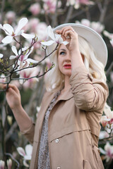 Magnolia flowers woman. A blonde woman wearing a white hat stands in front of a tree with pink...