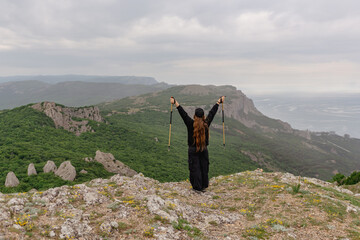 A woman stands on a mountain top, holding two poles and smiling