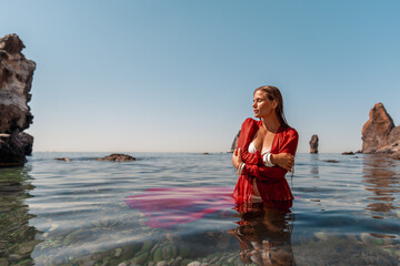 A woman in a red dress is sitting in the water. The water is clear and the sky is blue.