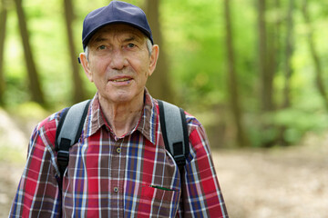 Portrait of an elderly man in a cap and plaid shirt in the forest