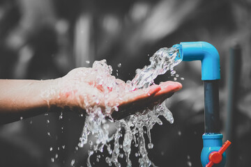 Close-up of a Hand Catching Fresh Water from a Blue Outdoor Faucet with a Blurred Natural Background