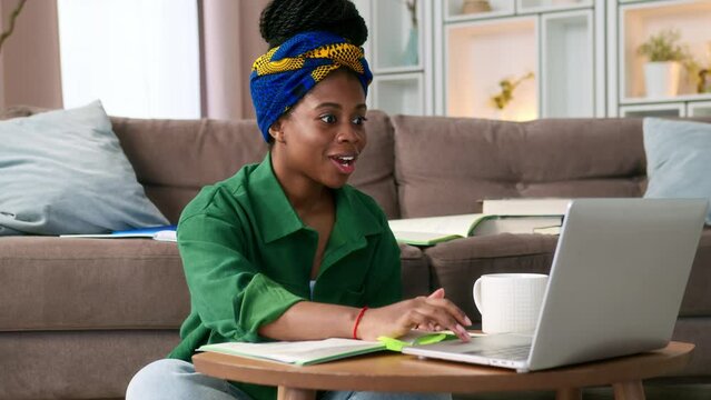 Young black woman freelancer at home working remotely on laptop. African American female student at online course. Exults, clap hands and rejoice due to received good feedback or passed exam