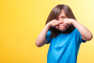 Boy with hands over his eyes crying. Blue T-shirt. Yellow background. Emotions. Space for text