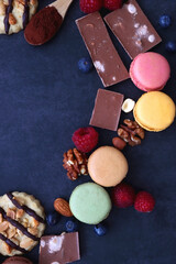 Macarons, chocolate, cookies, berries and various nuts on dark blue background. Top view.