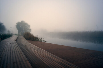 Autumn, early morning and thick fog, the river flows slowly, the banks are densely overgrown with...