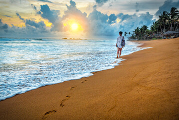 Woman with backpack walking on the tropical beach leaving footprints in the sand on Sri Lanka