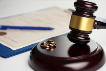 Marriage contract, golden wedding rings and gavel on white background, close-up