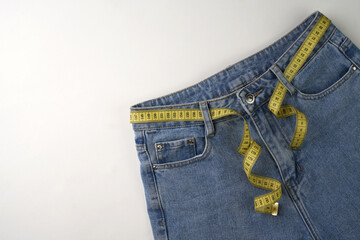 Jeans and measuring tape on a blue background with copy space, close-up. Weight loss and diet...