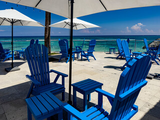Umbrella, sun lounger and chairs on a beach of fine white Caribbean sand full of beautiful palm trees and with the Caribbean Sea with crystal clear turquoise water in the background.