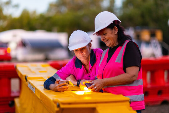 two female workers in hi vis and hard hats looking at their phones together