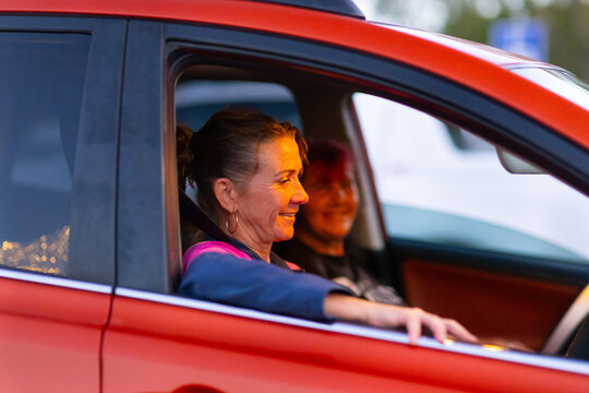 female driver of car with arm leaning out window with passenger blurred in background