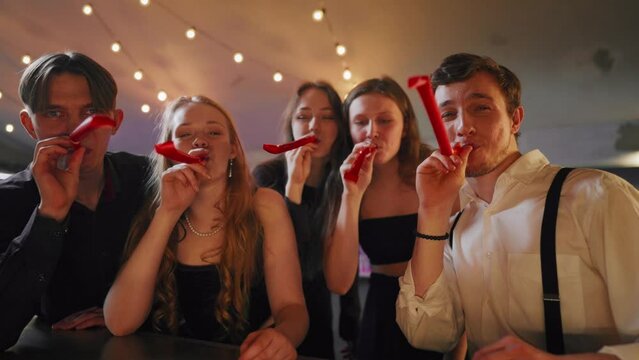 People celebrating b-day, blowing noisemakers whistles, congratulation party. Portrait of happy five best friends cheering and greeting, merry birthday party, gathering in festival in nightclub