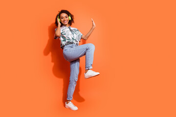 Fototapeta premium Photo portrait of brown wavy haired girl wear summer shirt listen audio playlist in bluetooth earphones dancing isolated on orange color background