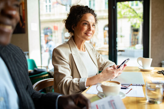 Professional woman using smartphone during business meeting in cafe