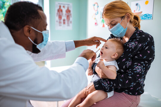 Pediatrician giving nasal vaccine to infant with mother wearing masks in clinic