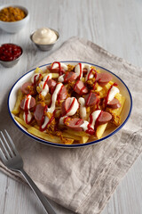 Homemade Salchipapa Fries with Ketchup, Mustard and Mayo on a Plate, side view.