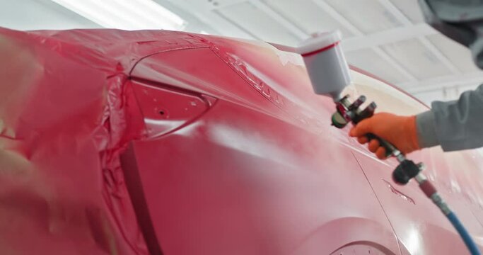 A professional worker spray painting a car red in a specialized car chamber at an auto repair shop. Quality automotive paint services and car body repair. Concept of automotive paint services