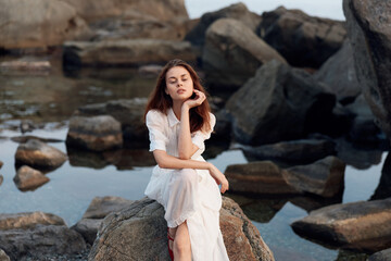 Serene woman in white dress contemplating by the water on a rocky shoreline