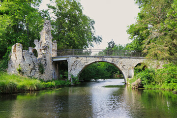 Fototapeta premium an ancient stone bridge and ruins over a tranquil river, surrounded by lush green trees. The scene combines historical charm with natural beauty, evoking a peaceful ambiance.