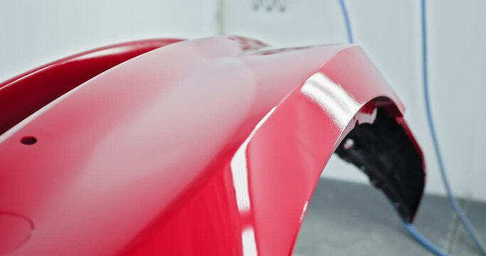 Close-up of a red car bumper being professionally painted in a specialized auto repair shop. Shiny and smooth finish. Car manufacturing factory. Automotive paint services, auto body shop concept
