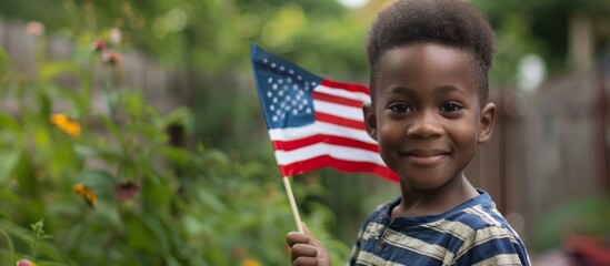 Happy little afro american boy holding American flag on blurred bokeh nature background, concept of celebration 4th of July