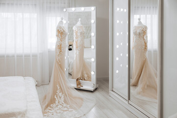 A bride's wedding dress is displayed in a bedroom with a large mirror. The dress is white and has a...