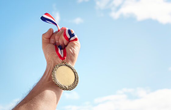 Gold medal held in athlete hand raised against sky background