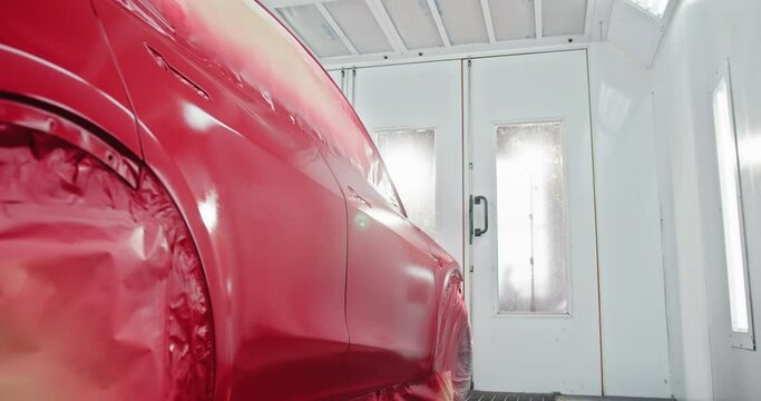 A automobile undergoing painting in a specialized paint chamber. The car is being coated with a fresh layer of red paint in a professional auto body shop. Car Being Painted in Automotive Paint Chamber