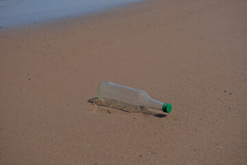An empty glass bottle is lying on the beach. environmental pollution