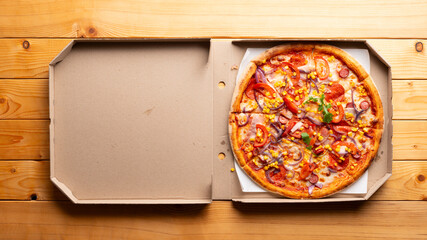 Pepperoni pizza with bell peppers sweetcorn and arugula in open carton box on natural wooden...