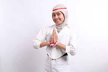 A friendly Indonesian muslim woman with red white flag ribbon gesturing traditional greeting to celebrate Indonesia Independence Day. Isolated by white background.