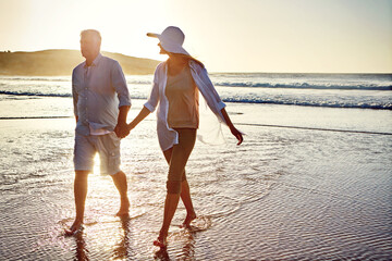 Senior couple, holding hands and walking with beach sunset for bonding, love or support together in...