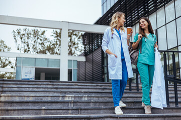 Two cheerful Caucasian women in healthcare attire enjoy a light conversation while descending...