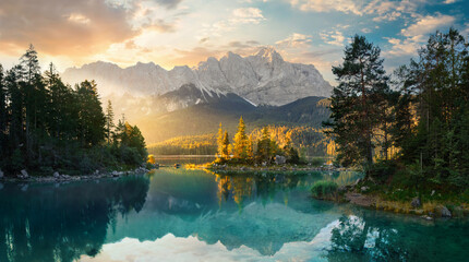 Painterly lake scenery in Germany with mountains reflected in the teal water and a beautiful ray of morning sunlight illuminating some trees 