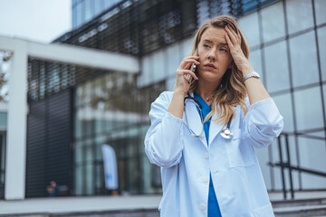 A concerned Caucasian female healthcare worker in a lab coat uses her smartphone, possibly...