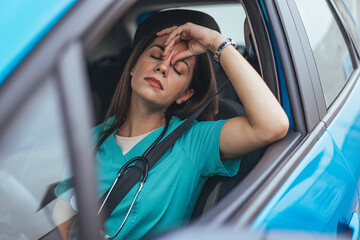 A fatigued Caucasian female nurse sits in her car, eyes closed, with hand on forehead, reflecting...
