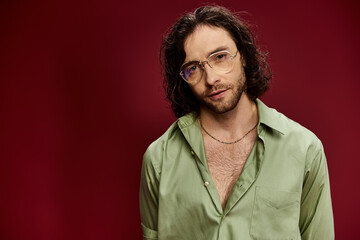 Fototapeta premium A handsome man wearing glasses and a green silk shirt poses against a vibrant red background.